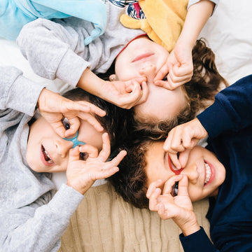 Three children lying down making fun glasses shapes with their fingers
