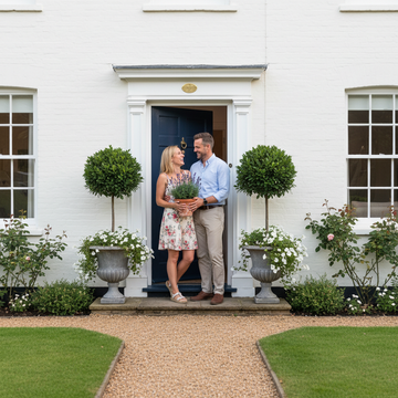 Couple at freshly painted front door with potted plants improving curb appeal on a budget