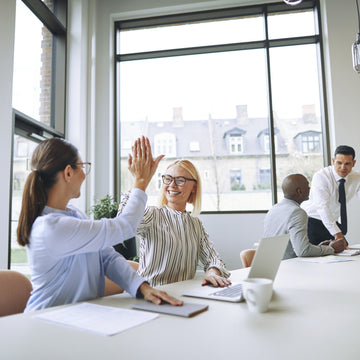 Two women high-fiving across a conference table in a bright modern office