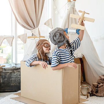 Two children playing inside a cardboard box aeroplane with homemade playroom wall decor