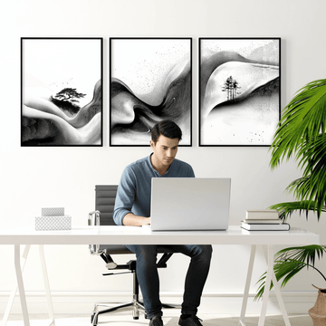 Man working at desk beneath three black and white abstract landscape prints, home office artwork ideas