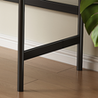 Close-up of a black metal chair leg on a wooden floor with a plant leaf in the corner.