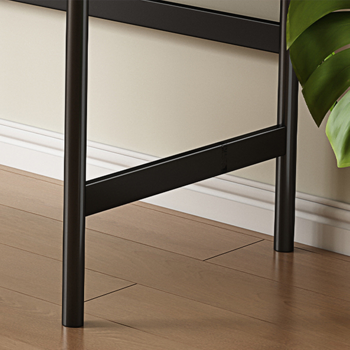 Close-up of a black metal chair leg on a wooden floor with a plant leaf in the corner.