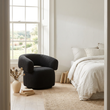 Oliveto black boucle swivel armchair beside a bedroom window in a wide room view