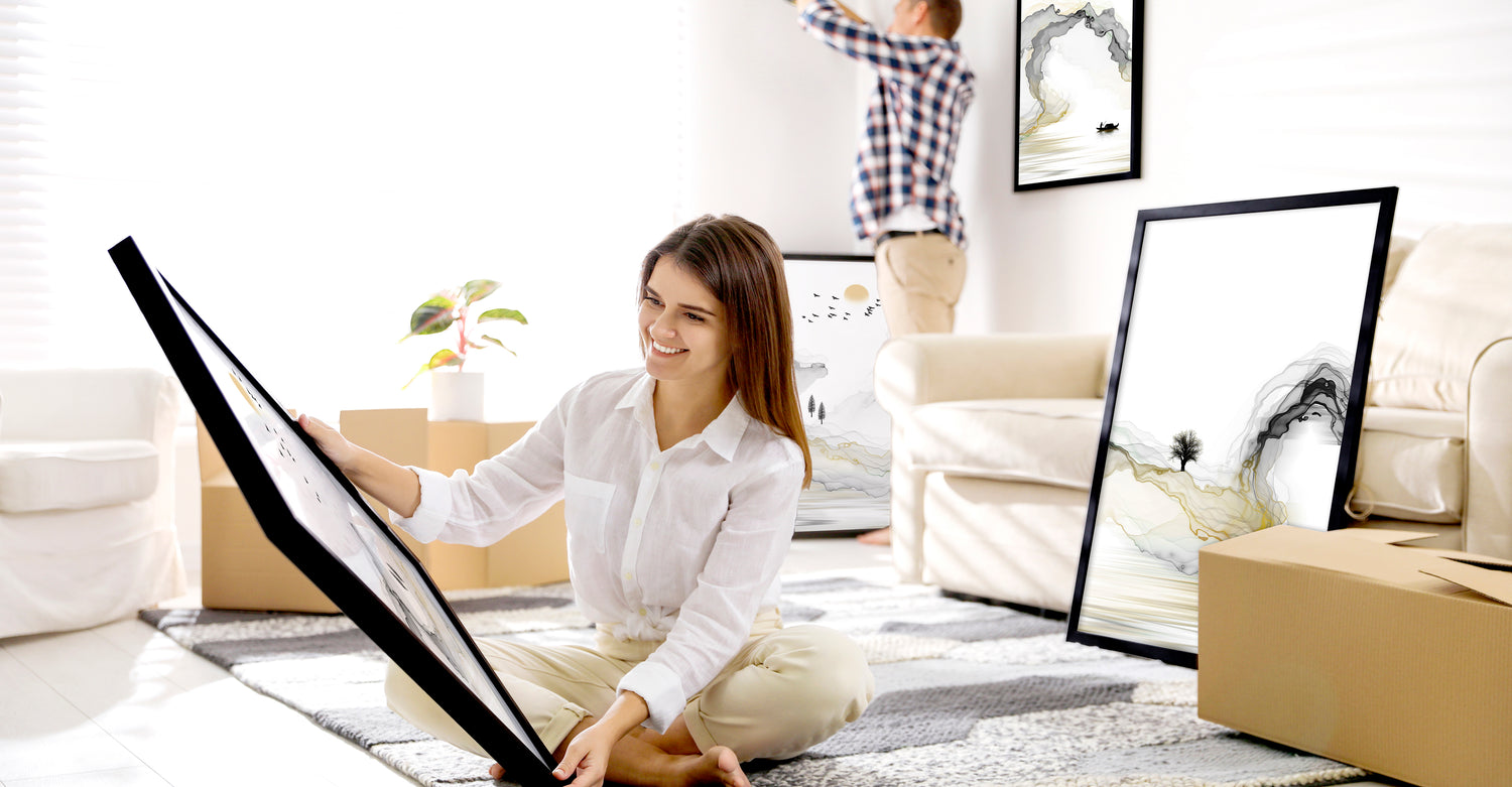 Woman arranging framed landscape wall art pictures in a bright living room